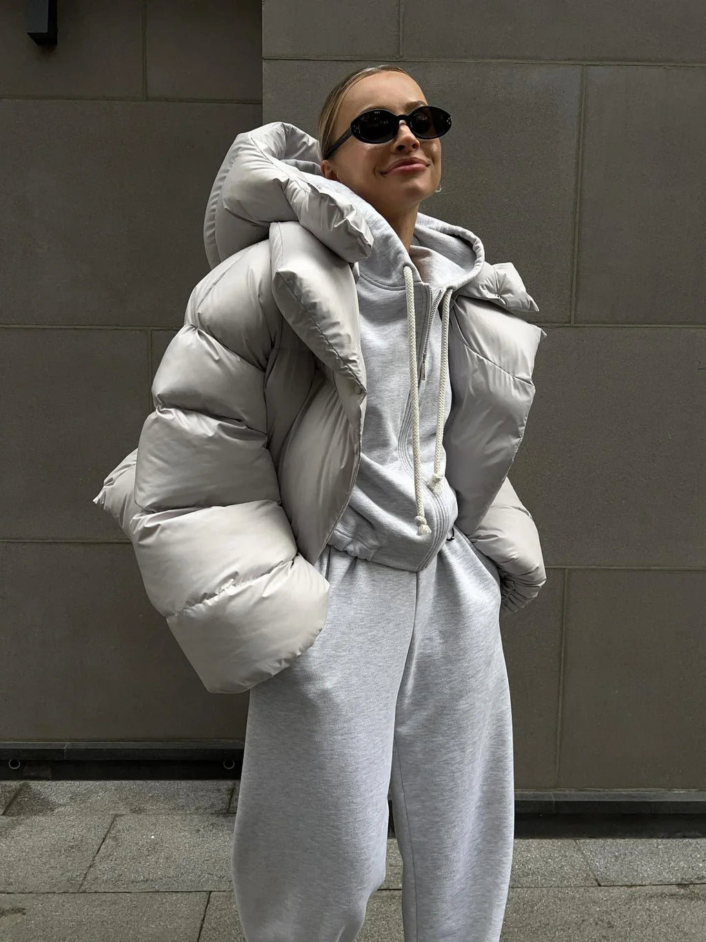Woman wearing a light grey oversized hooded puffer jacket with a cropped length and snap button closure.