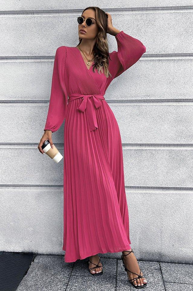 Woman in a pink pleated maxi dress with a v-neck, holding a coffee cup.