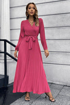 Woman wearing a long sleeve pink pleated maxi dress with a v-neck and a self-tie belt.