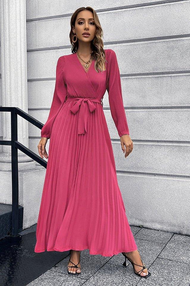 Woman wearing a long sleeve pink pleated maxi dress with a v-neck and a self-tie belt.