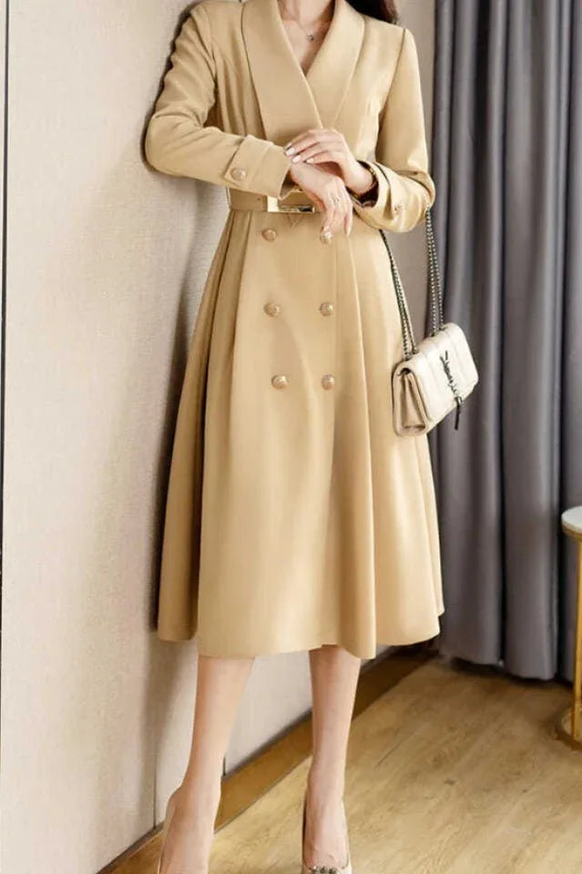 woman standing in a beige coat dress with a flared skirt, showcasing the belted waist and double-breasted design