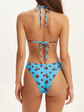 Rear view of a woman in a light blue floral print bikini, showing the tie-back halter top and high-cut bottoms.