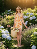 Woman walking in a garden with a straw bag, wearing a sleeveless floral print mini dress.