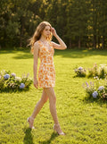 Woman walking in a grassy field wearing a sleeveless floral print mini dress.