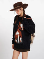 Close-up profile of a woman wearing a black fuzzy knit sweater with a brown and white horse graphic, brown cowboy hat, and brown boots.
