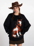 Front view of a woman wearing a black fuzzy knit sweater with a detailed brown and white horse graphic on the front, styled with a brown cowboy hat.