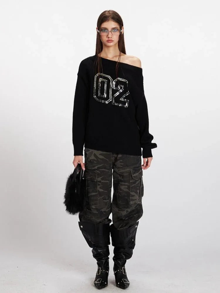 Woman wearing a black off-the-shoulder knit sweater with sequined numbers '02' on the front, paired with camouflage cargo pants and black boots.