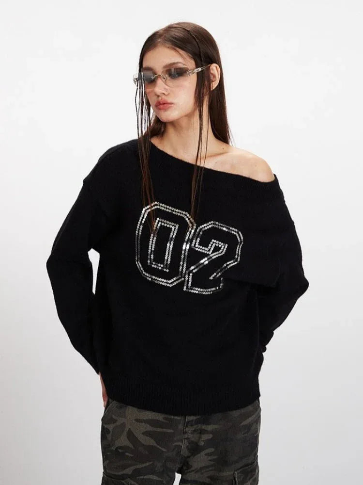 Woman wearing a black off-the-shoulder knit sweater with sequined numbers '02' on the front, looking at the camera.