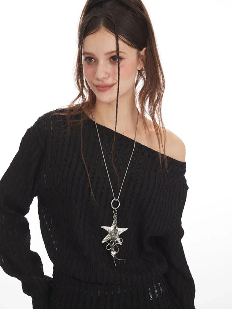Detail of a woman's black off-the-shoulder knit sweater with a star pendant necklace.