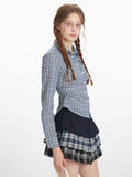 Side profile of a woman wearing a blue and white plaid button-down shirt with a dark navy ruffled skirt and a plaid mini skirt