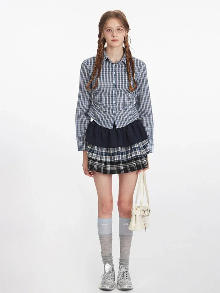 Woman wearing a blue and white plaid button-down shirt with a dark navy ruffled skirt and a plaid mini skirt