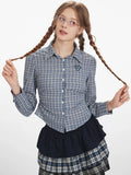 Woman wearing a blue and white plaid button-down shirt and a plaid skirt, posing with her hair braids