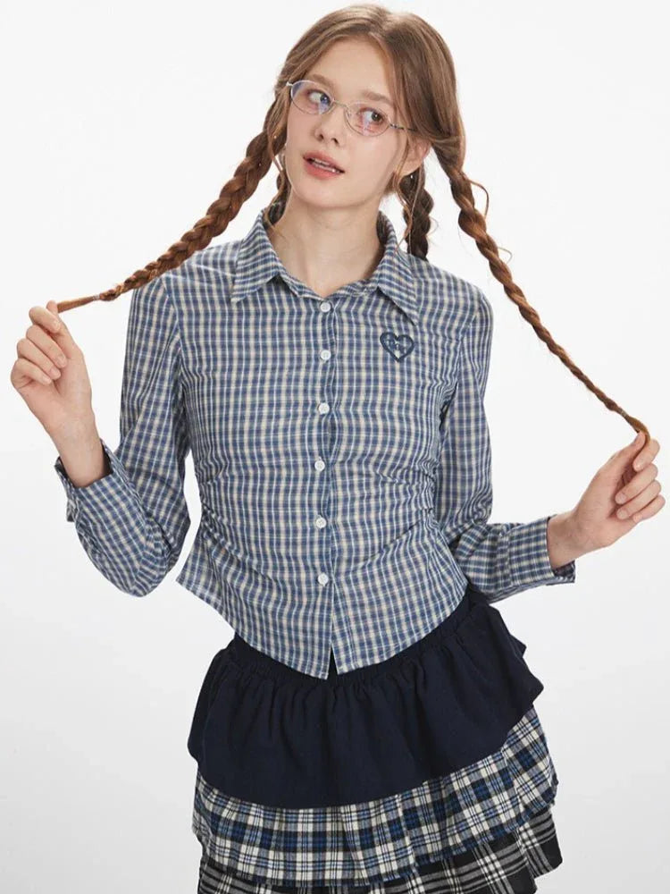 Woman wearing a blue and white plaid button-down shirt and a plaid skirt, posing with her hair braids