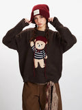Woman adjusting her red beanie while wearing a brown knit sweater with a teddy bear graphic and brown pants.