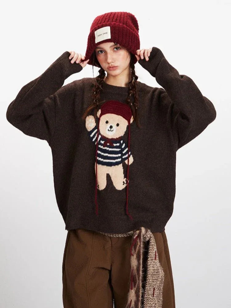Woman adjusting her red beanie while wearing a brown knit sweater with a teddy bear graphic and brown pants.