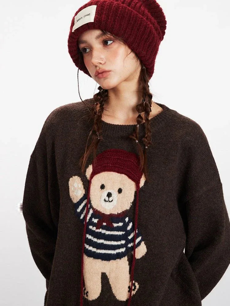 Close-up of a woman wearing a brown knit sweater with a teddy bear graphic and a red beanie.