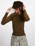 Model adjusting a brown cap while wearing a brown collared knit top.