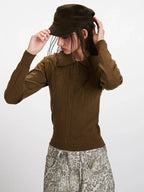 Model adjusting a brown cap while wearing a brown collared knit top.