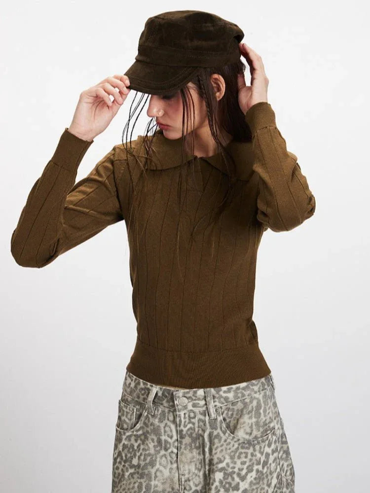Model adjusting a brown cap while wearing a brown collared knit top.