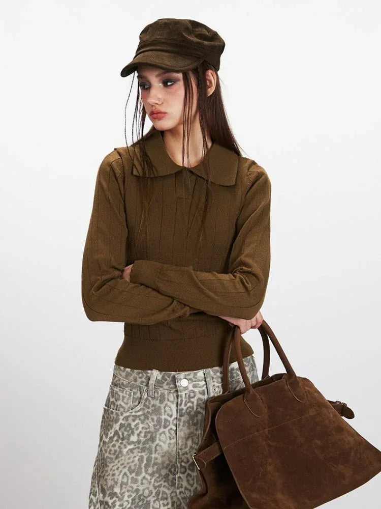 Close-up of a model in a brown collared knit top, arms crossed, holding a brown handbag.