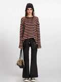 Woman wearing a maroon and cream striped long-sleeve knit sweater with a relaxed fit, black pants, and a black beanie.