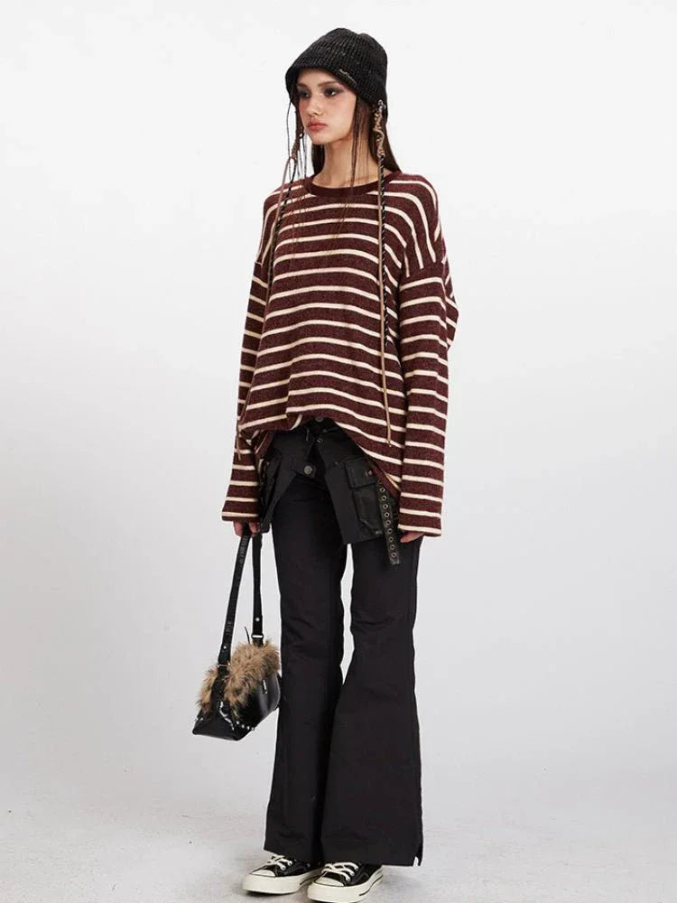 Full body shot of a woman in a maroon and cream striped knit sweater and black pants, holding a small black bag with faux fur accents.