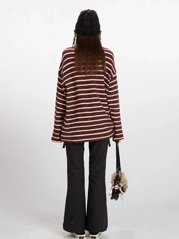Woman wearing a maroon and cream striped long-sleeve knit sweater with a relaxed fit, black pants, and a black beanie.