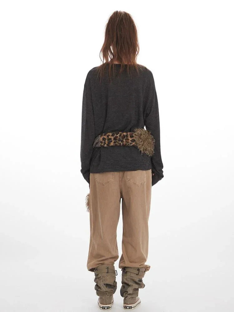 Woman wearing a dark gray long-sleeve v-neck top with a leopard print and faux fur scarf accessory, and tan wide-leg pants.