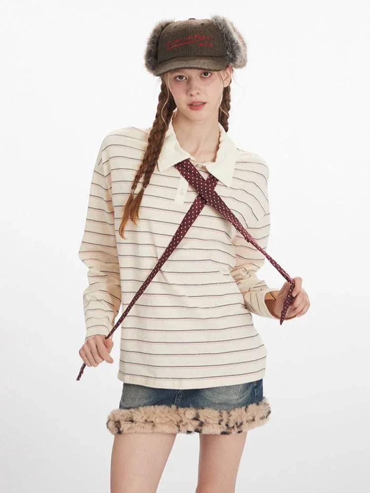 Woman holding the ends of a dark red polka dot tie worn with a cream and dark stripe long sleeve polo shirt and a denim mini skirt with fur trim.