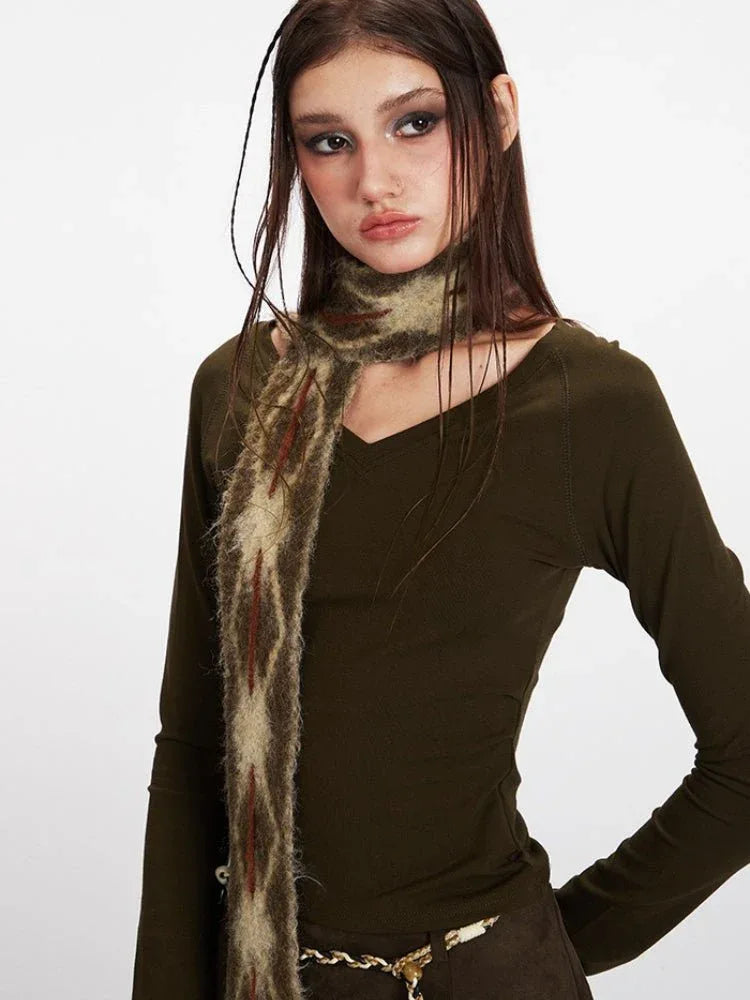 Front view of a woman wearing a long sleeve olive green top and a patterned scarf, styled with a gold chain belt.