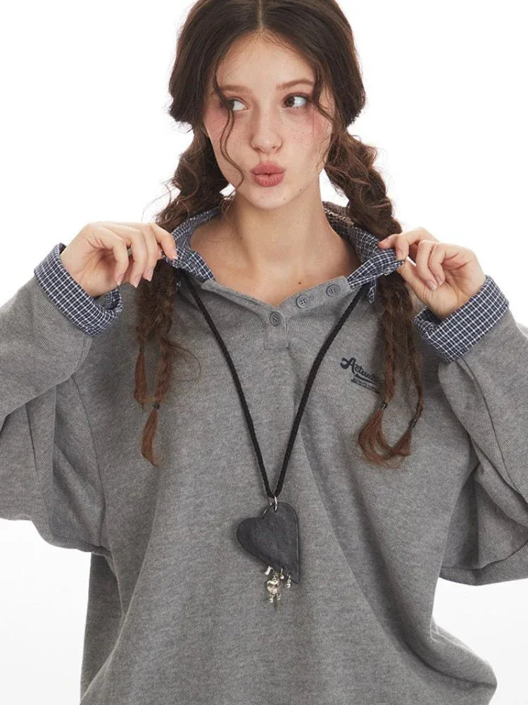 Close-up of a woman adjusting the plaid collar of her grey sweatshirt, wearing a heart pendant necklace.