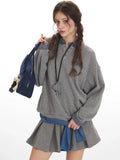Close-up of a woman wearing a grey oversized sweatshirt over a plaid collared shirt, showing the layered detail and embroidered logo.