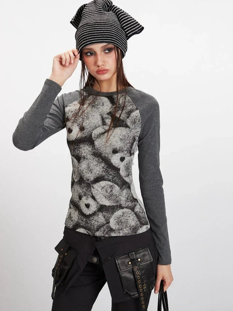 Woman adjusting her beanie while wearing a grey long-sleeve top with a teddy bear print.