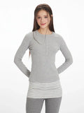 Front view of the model smiling, showcasing the grey long-sleeve top with button placket and striped hem detail.