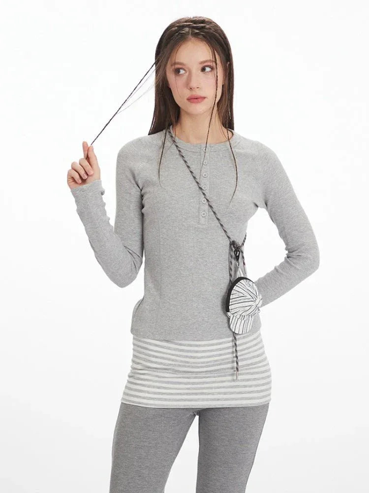Close-up of the model's face and upper body, showing the grey long-sleeve top with button detail and striped accent.