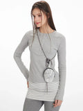 Model posing with a small crossbody bag, wearing a grey long-sleeve top and grey flared pants.