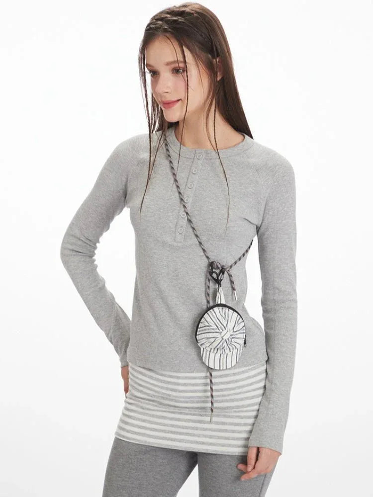 Model posing with a small crossbody bag, wearing a grey long-sleeve top and grey flared pants.