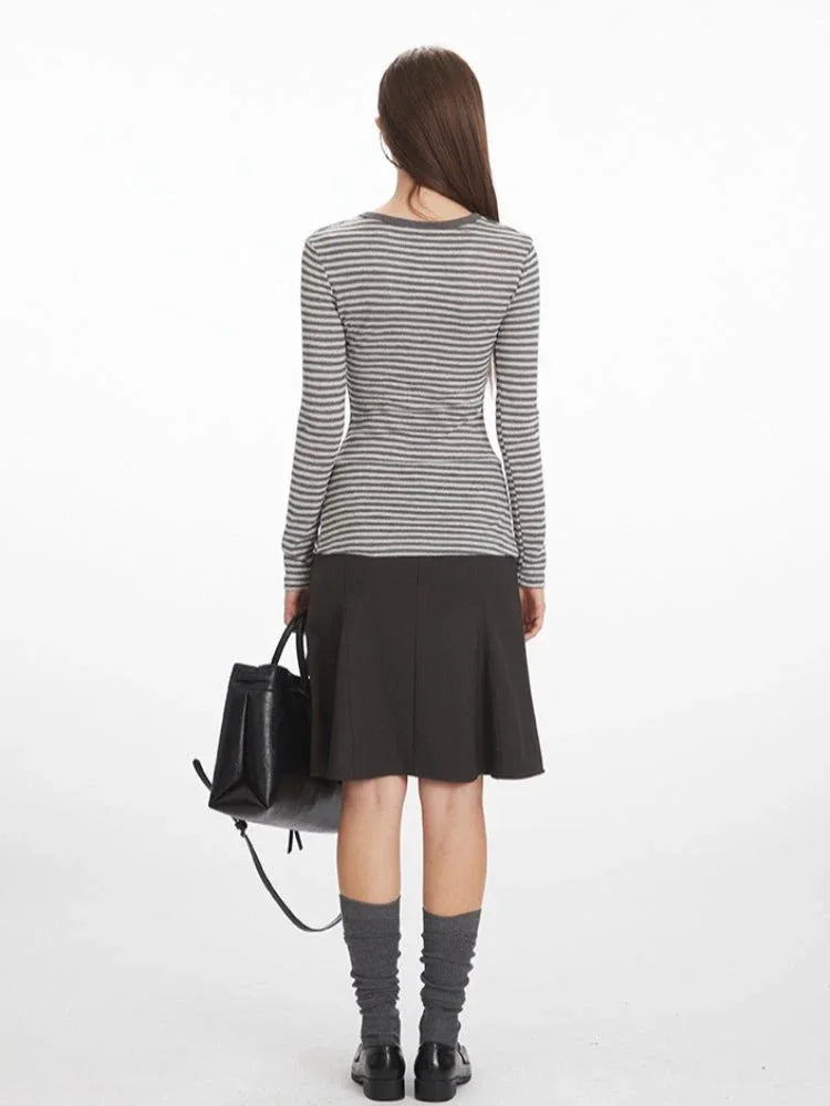 Woman wearing a grey and white striped long-sleeve top with a button-up placket and embroidered detail, paired with a dark grey A-line skirt, grey knee-high socks, and black loafers.