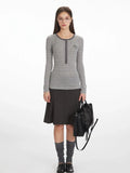 Woman wearing a grey and white striped long-sleeve top with a button-up placket and embroidered detail, paired with a dark grey A-line skirt, grey knee-high socks, and black loafers.