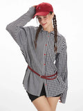 Woman with braided hair wearing a red baseball cap and an oversized black and white gingham shirt with a contrasting pattern and red belt.