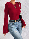 Close-up of a woman's torso wearing a red ribbed knit top with flared sleeves.