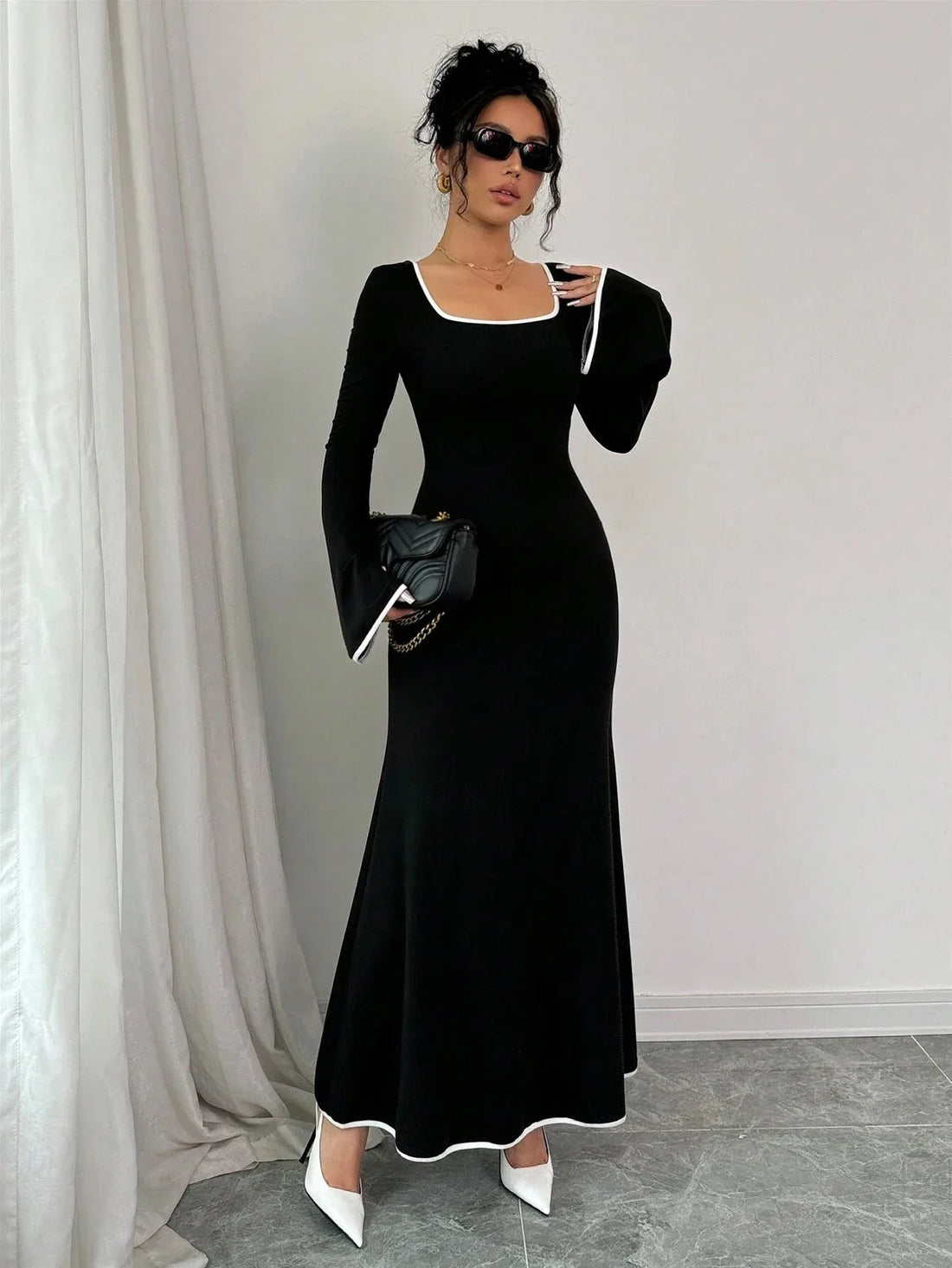 Woman wearing a black maxi dress with white contrast piping and bell sleeves.
