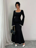Full length shot of a woman in a black maxi dress with white contrast piping and bell sleeves.