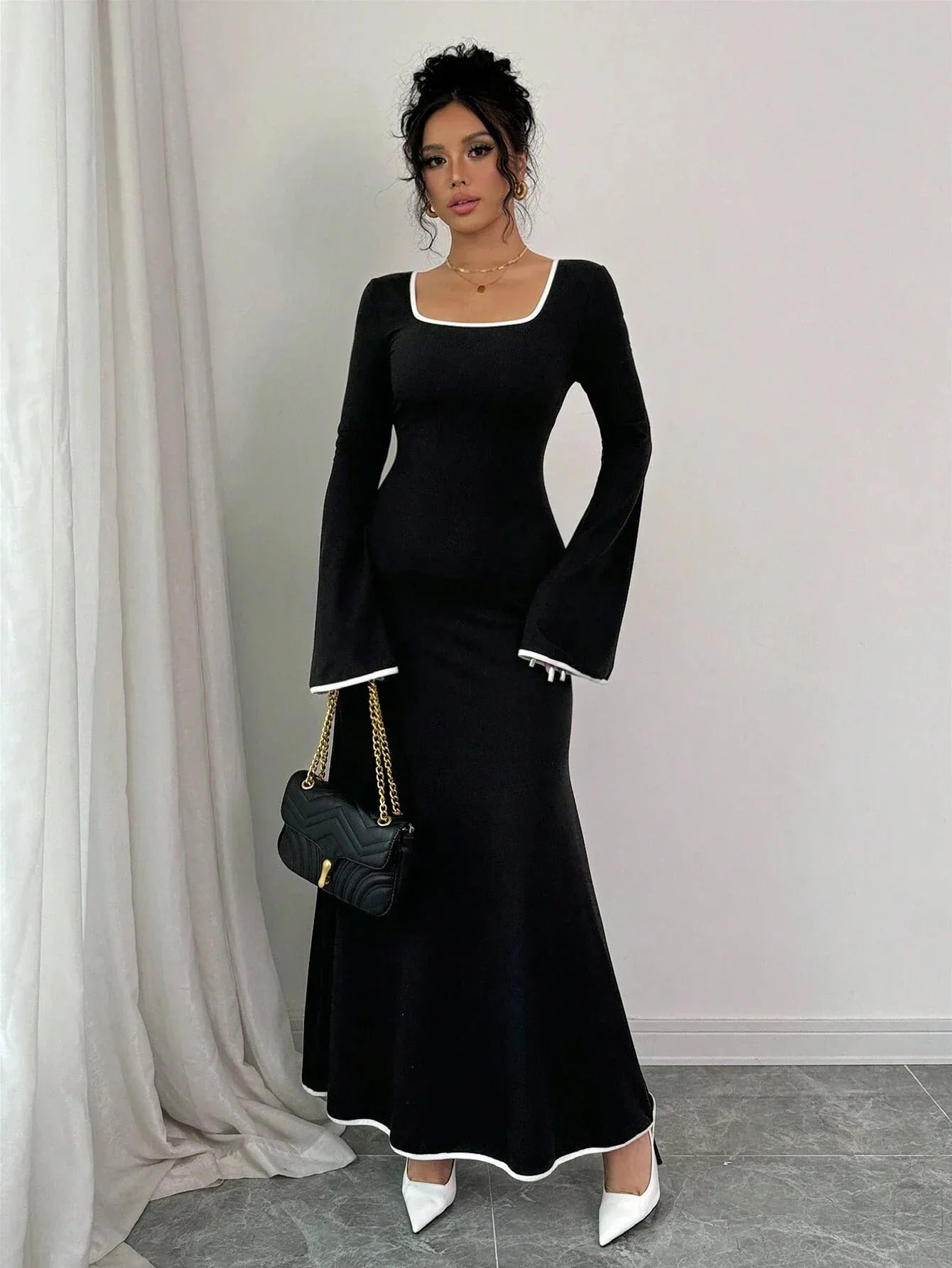 Full length shot of a woman in a black maxi dress with white contrast piping and bell sleeves.