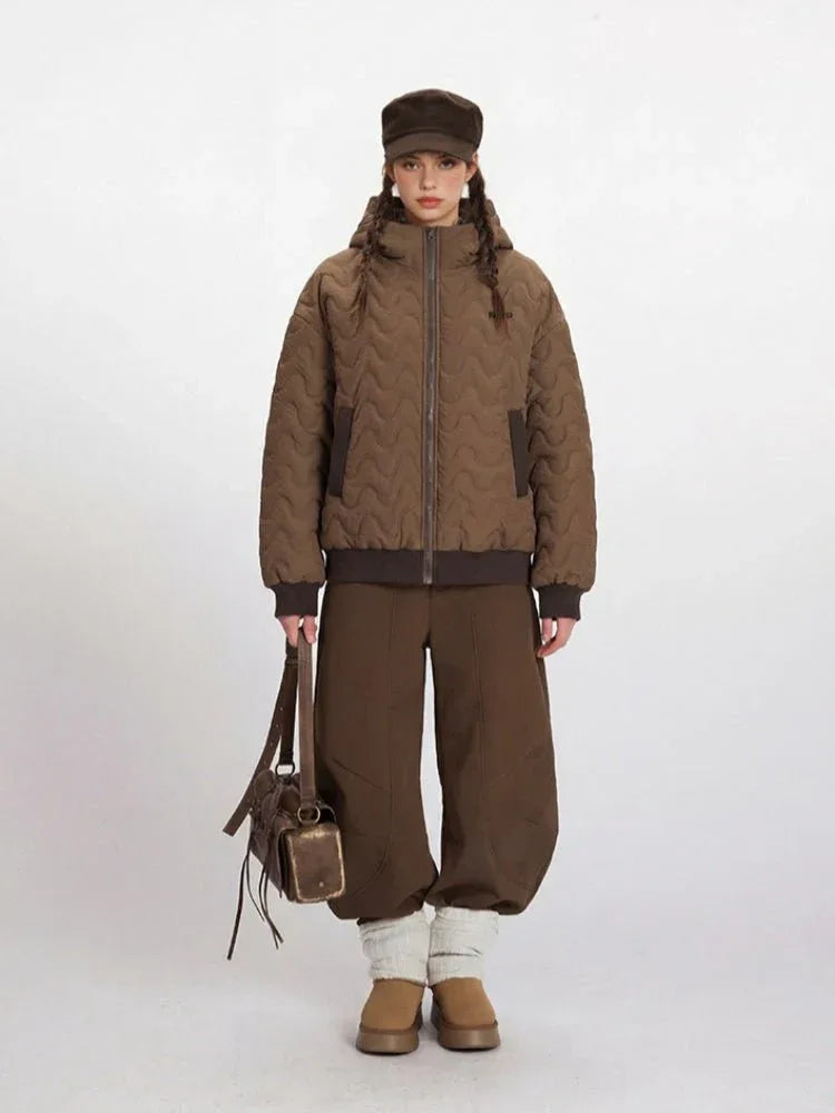 Woman wearing a brown quilted bomber jacket with a hood, brown pants, and a brown cap.