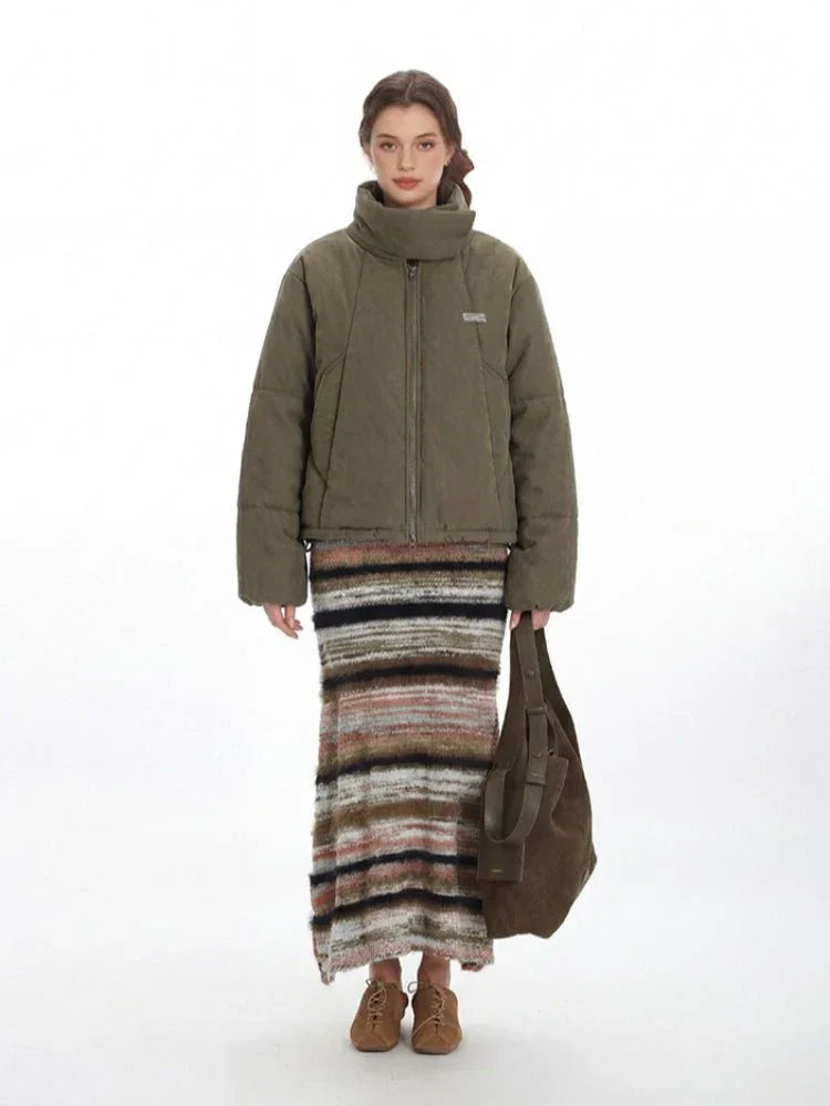 Woman wearing a green quilted puffer jacket with a high funnel neck and zipper closure, paired with a striped maxi skirt. Main image
