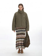 Woman wearing a green quilted puffer jacket with a high funnel neck and zipper closure, paired with a striped maxi skirt.