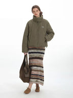 Model holding a brown tote bag while wearing a green puffer jacket and striped skirt.