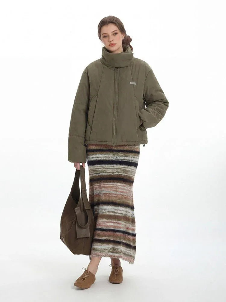 Model holding a brown tote bag while wearing a green puffer jacket and striped skirt.