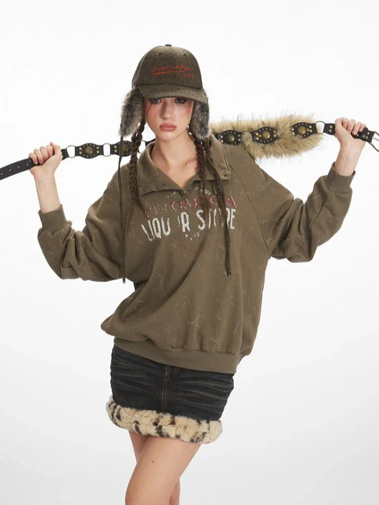 Woman wearing a green graphic print sweatshirt and black denim skirt with fur trim, holding a decorative belt over her shoulders.